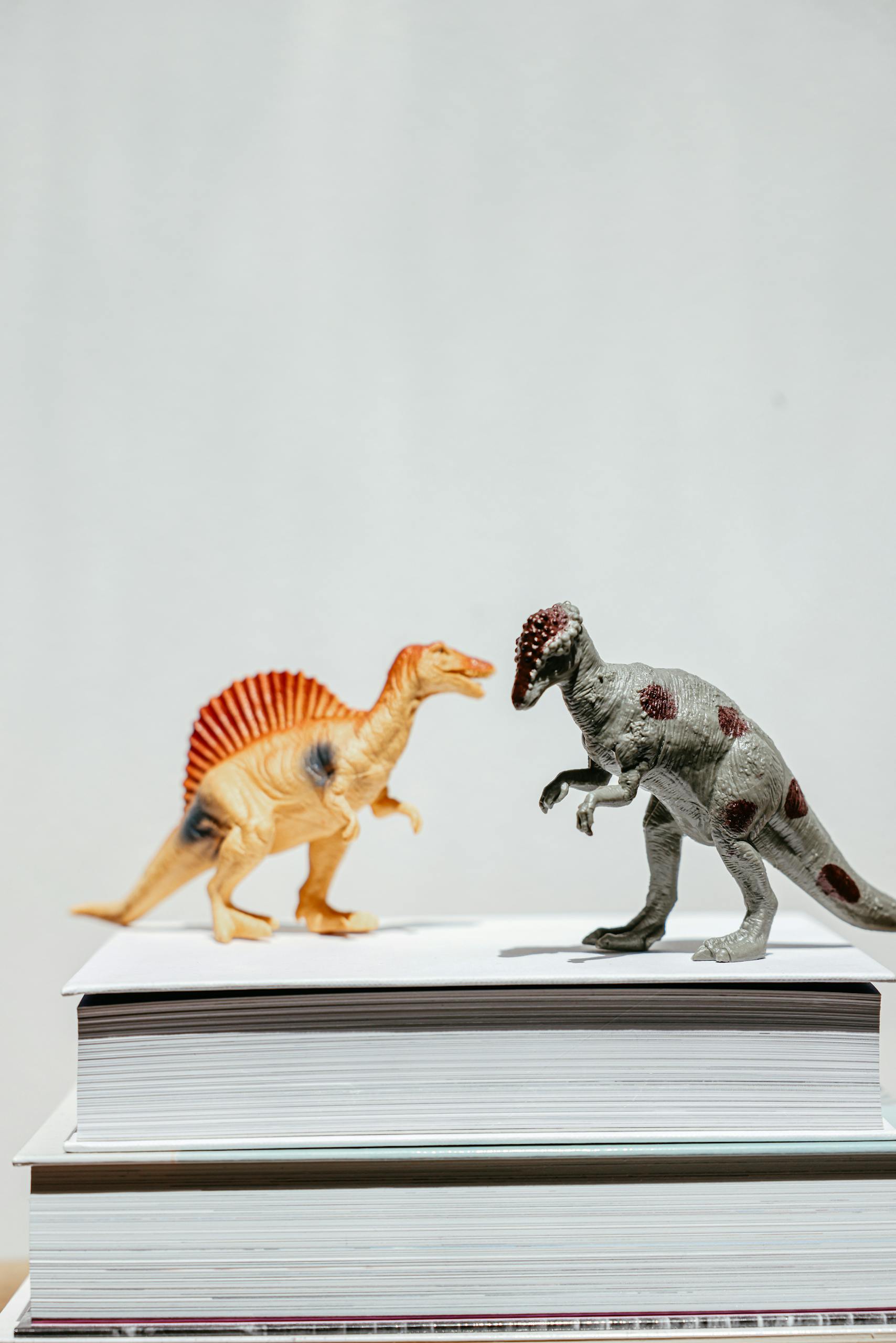 Colorful dinosaur toys displayed on stacked books against a plain backdrop, ideal for educational or play themes.